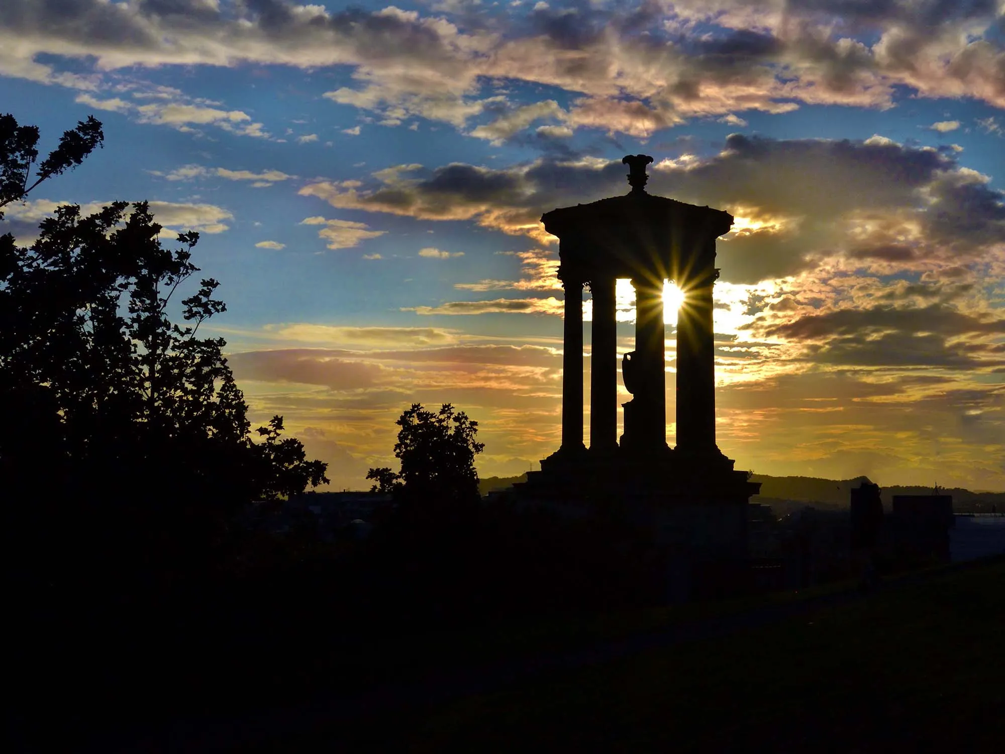 Silhouette of the Dugald Stewart Monument on Calton Hill with the sun bursting through an arch